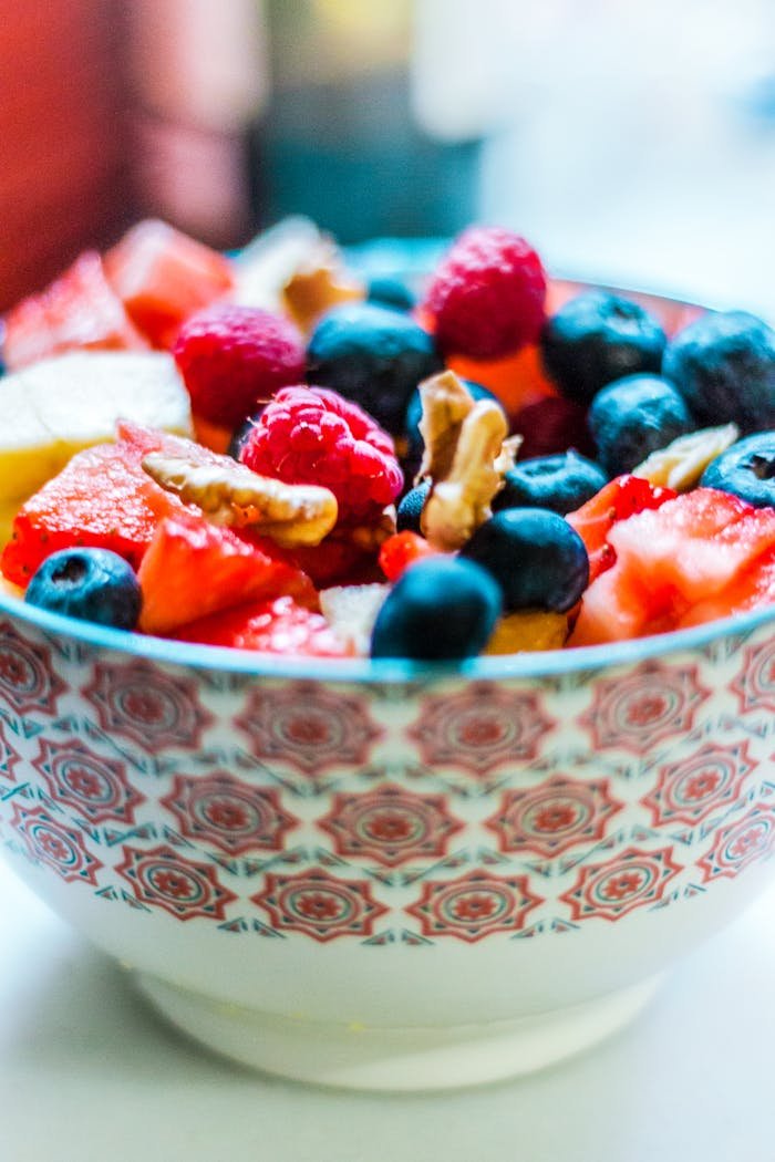Colorful fruit salad in a decorative bowl with fresh berries and nuts, perfect for a healthy and organic snack.