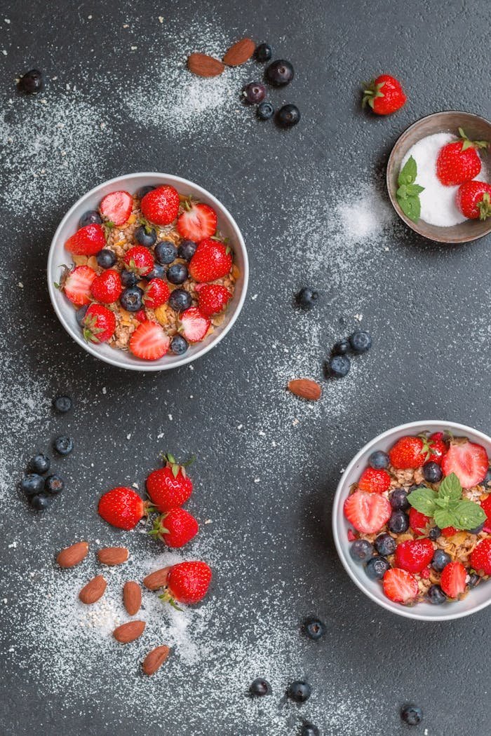 Top view of fresh berry and nut muesli bowls on a dark background.