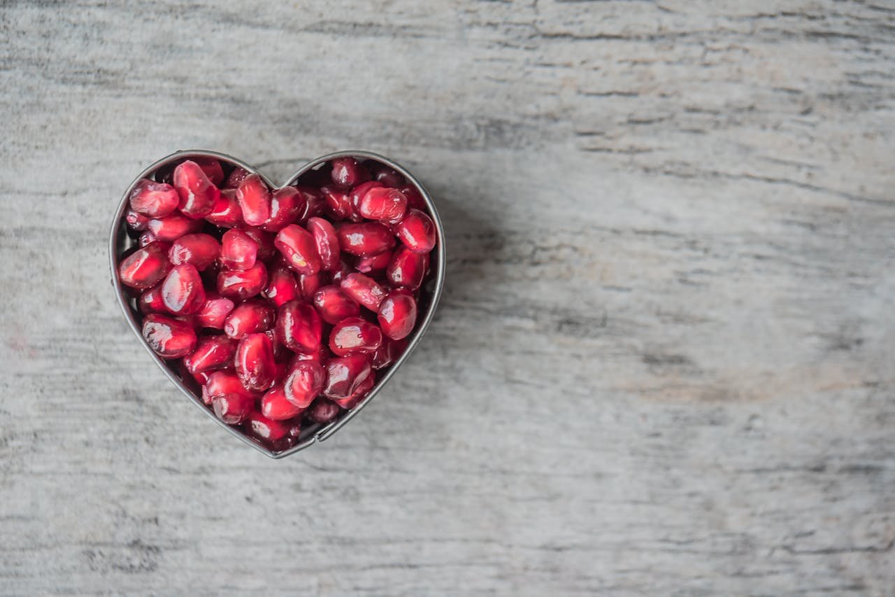 🌱 Fibremaxxing & Personalized Nutrition: The 2025 Health Trends You Can’t Ignore Delicious and juicy pomegranate seeds in a heart-shaped bowl on a wooden table.